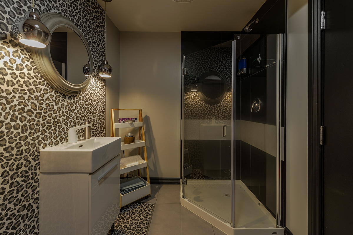 regular room with leopard ceramic wall a sink and a glass shower